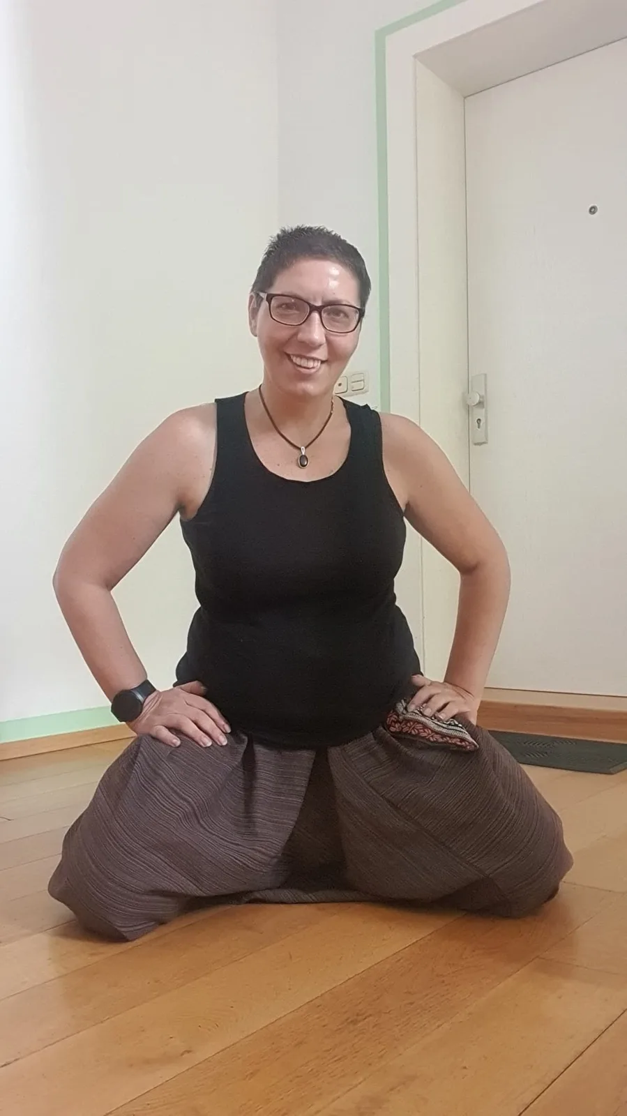 Sina Riegel lächelt und sitzt in einer weiten Hose auf dem Boden